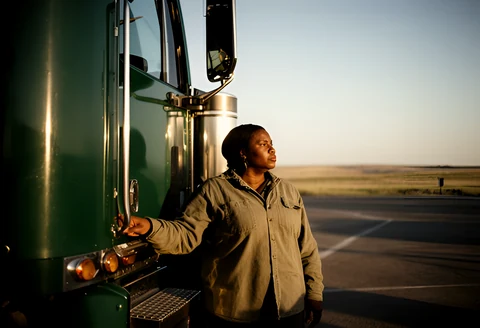 Owner-operator truck driver standing beside her rig at golden hour